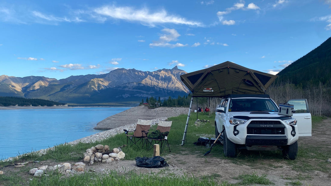 White 5th Gen Toyota 4Runner with rooftop tent camped beside a mountain lake